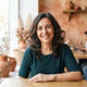 A smiling middle-aged woman posing for a portrait in a bright, modern indoor setting with warm decorative accents.