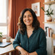 Portrait of a happy Spanish woman smiling in a bright home office setting with warm terracotta and sienna decor.