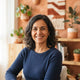 Portrait of a smiling Spanish woman in a sunlit home interior with terracotta decor, representing a satisfied wellness custom